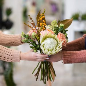 Safe and quick flower bouquet delivery for someone you love. Women hands holding a creative arrangement of roses dahlia and berries